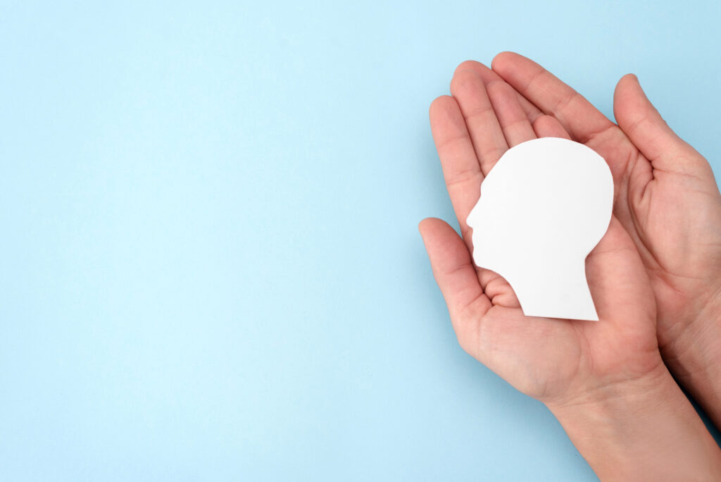 Hands holding paper human head silhouette on blue background